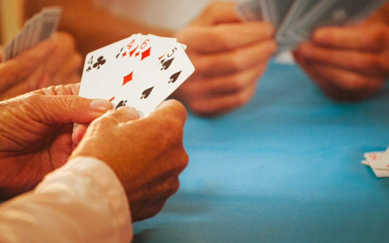 Een tafel waarboven handen zichtbaar zijn met spelkaarten daarin.
